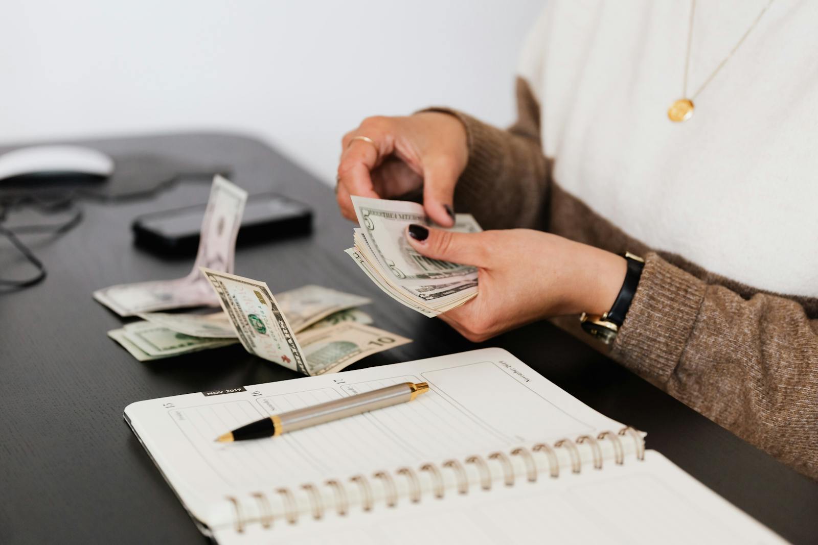 Person counting cash next to a budget notebook